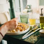 Hand pointing at pasta and drinks on a green table.